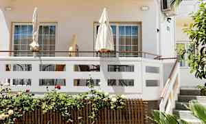 Terassi, jossa on aurinkovarjoja ja ulkokalusteita vaalean rakennuksen edessä. (Tekoälyn luoma teksti)