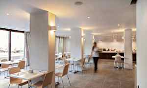 Valoisa ja moderni ruokailutila, jossa on valkoiset pöydät ja vaaleat puutuolit. (Tekoälyn luoma teksti)