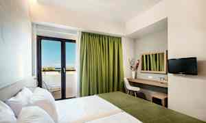 Hotellihuone, jossa on kaksi sänkyä, työskentelytila peilillä, tuoli ja seinälle asennettu televisio. Huoneessa on parveke ja vihreät verhot, näkymä merelle. (Tekoälyn luoma teksti)