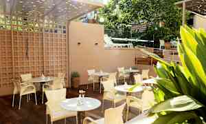 Terassi, jossa on pöytiä ja tuoleja, ympäröitynä vehreydellä. (Tekoälyn luoma teksti)