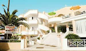 Rakennus, jossa valkoinen julkisivu ja kierreportaat, ympärillä vehreyttä ja kyltti, jossa lukee 'Rita Suites'. (Tekoälyn luoma teksti)