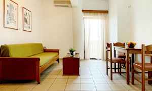 Olohuone, jossa on sohva, sohvapöytä ja ruokapöytä tuoleineen. Vaaleat seinät ja verhot. (Tekoälyn luoma teksti)