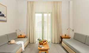 Olohuone, jossa on kaksi harmaata sohvaa, pöytä hedelmäkorilla ja kirjalla sekä verhot ikkunan edessä. (Tekoälyn luoma teksti)