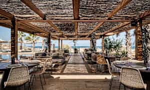 Ulkoterassi, jossa puupöytiä ja -tuoleja katoksen alla, näkymä merelle. (Tekoälyn luoma teksti)