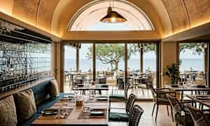 Ravintola, jossa näkymä merelle, huonekalut puusta ja lasiyksityiskohtia. (Tekoälyn luoma teksti)