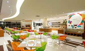 Ruokailutila, jossa on värikkäitä tuoleja ja katettuja pöytiä sekä tarjoilupöytä taustalla. (Tekoälyn luoma teksti)