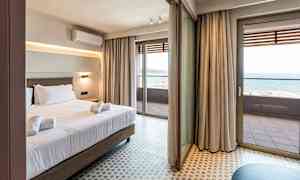 Hotellihuone, jossa sänky ja pyyhkeet. Suuret lasiovet johtavat parvekkeelle, jolta näkyy meri. (Tekoälyn luoma teksti)