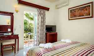 Hotellihuone, jossa on sänky, televisio, meikkipöytä ja parveke näkymällä palmupuun suuntaan. (Tekoälyn luoma teksti)