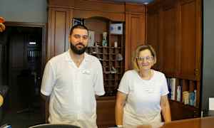 Kaksi henkilöä seisoo vastaanottotiskin ääressä, taustalla puisia paneeleja. (Tekoälyn luoma teksti)