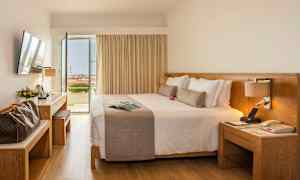 Hotellihuone, jossa on suuri parivuode, työpöytä ja avoimet ovet parvekkeelle näkymällä. (Tekoälyn luoma teksti)