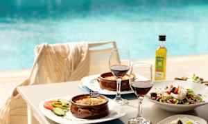 Lautasia kreikkalaisilla ruoilla, kaksi lasillista punaviiniä ja uima-allas taustalla. (Tekoälyn luoma teksti)