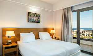 Huone, jossa on kaksi erillistä vuodetta, pöytävalaisimia ja ikkunaoovi, joka avautuu merelle. (Tekoälyn luoma teksti)