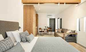 Hotellihuone, jossa on parisänky etualalla, puusisustus ja pieni istuma-alue, jossa pöytä ja kaksi tuolia taustalla. (Tekoälyn luoma teksti)