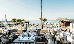 Ulkoterassi, jossa pöytiä ja tuoleja, taustalla merinäköala ja ranta. (Tekoälyn luoma teksti)