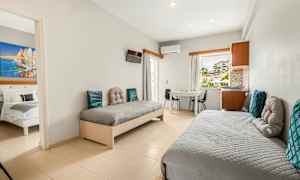 Hotellihuone, jossa kaksi yhden hengen vuodetta, pöytä ja tuolit, sekä näkymä ikkunan läpi. (Tekoälyn luoma teksti)