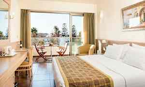 Hotellihuone, jossa parivuode, kirjoituspöytä, istuimia ja parveke, jossa kaksi tuolia ja pöytä. (Tekoälyn luoma teksti)