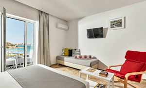 Hotellihuone, jossa oleskelutila, sänky ja näkymä rannalle lasioven kautta. (Tekoälyn luoma teksti)