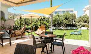 Terassi, jossa on pöytiä, tuoleja ja riippumatoja, nurmikon ja puiden ympäröimänä. (Tekoälyn luoma teksti)