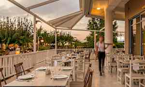 Ulkoterassi katettujen pöytien kanssa katoksen alla, ympäröitynä vehreydellä. (Tekoälyn luoma teksti)