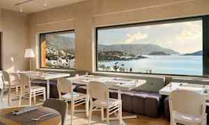 Ravintola, jossa on katettuja pöytiä ja panoraamanäkymä rannikkoon ja vuoriin. (Tekoälyn luoma teksti)