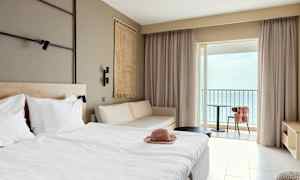 Hotellihuone, jossa on sänky, sohva ja parveke merinäköalalla. (Tekoälyn luoma teksti)