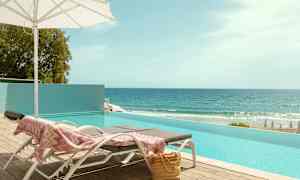 Aurinkotuolit uima-altaan reunalla ja merinäkymä. (Tekoälyn luoma teksti)