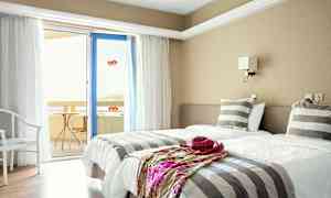 Hotellihuone, jossa on kaksi erillistä vuodetta, raidalliset vuodevaatteet ja ovi parvekkeelle. (Tekoälyn luoma teksti)