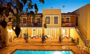 Huoneistokompleksi, jonka etualalla on uima-allas, ympäröitynä terrakotanvärisillä rakennuksilla ja kasvillisuudella. (Tekoälyn luoma teksti)