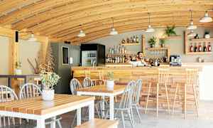 Kahvila, jossa on puusisustus, pöytiä, tuoleja ja baaritiski. (Tekoälyn luoma teksti)