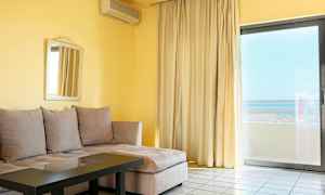 Olohuone, jossa beige kulmasohva, lasipöytä, peili seinällä ja suuret ikkunaverhot näkymällä. (Tekoälyn luoma teksti)