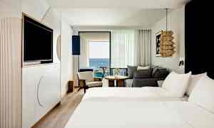 Hotellihuone, jossa on kaksi vuodetta, istumapaikkoja ja parveke merinäköalalla. (Tekoälyn luoma teksti)