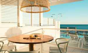 Ulkoalue, jossa pöytä ja tuolit, merinäkymä taustalla. (Tekoälyn luoma teksti)