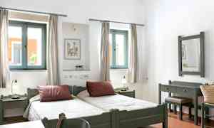 Valokuva vaaleasta makuuhuoneesta, jossa on kaksi erillistä vuodetta, ikkunat valon sisääntulolla ja puukalusteet. (Tekoälyn luoma teksti)