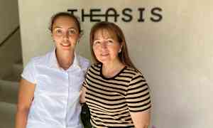 Kaksi henkilöä seisoo seinän edessä, jossa on logo. (Tekoälyn luoma teksti)