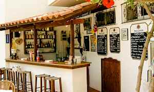 Pieni ulkobaari, jossa on puutuoleja, juomapulloja hyllyillä ja ruokalistat seinällä. (Tekoälyn luoma teksti)