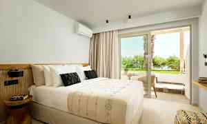 Valoisan hotellihuoneen sisustus, jossa on parivuode ja pieni istuinryhmä ulkopuolella näkymällä vehreään. (Tekoälyn luoma teksti)