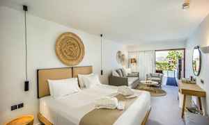 Moderni hotellihuone, jossa suuri sänky, istuinryhmä ja näkymä uima-altaalle lasiovien läpi. (Tekoälyn luoma teksti)