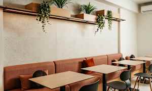 Moderni kahvila-alue, jossa punaiset sohvat ja puupöydät, koristeena roikkuvia kasvialtaita yllä. (Tekoälyn luoma teksti)