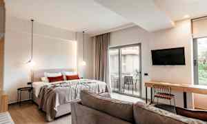 Nykyaikainen hotellihuone, jossa on sänky, sohva, kirjoituspöytä, televisio ja parveke. (Tekoälyn luoma teksti)