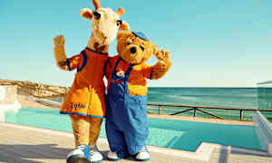 Kaksi maskottia, kirahvi ja karhu, seisovat uima-altaan vierellä ja vilkuttavat. (Tekoälyn luoma teksti)