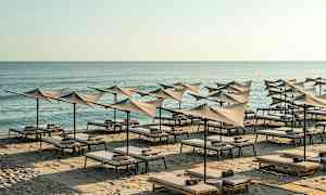 Ranta, jossa aurinkotuoleja ja varjoja meren äärellä. (Tekoälyn luoma teksti)