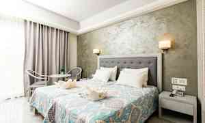 Hotellihuone, jossa on parivuode, yöpöytä, koristeellinen päiväpeite ja istuinryhmä. (Tekoälyn luoma teksti)