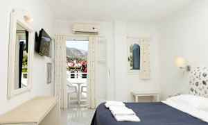 Hotellihuone, jossa on sänky, seinällä oleva televisio ja parveke, jolta on näkymät vuoristoon. (Tekoälyn luoma teksti)