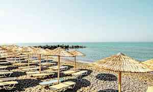 Ranta, jossa aurinkotuoleja ja aurinkovarjoja rauhallisen meren edessä. (Tekoälyn luoma teksti)