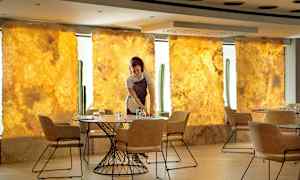 Tarjoilija kattaa pöydän tyylikkäässä ravintolassa, jonka tausta on kultainen ja tuolit modernit. (Tekoälyn luoma teksti)