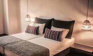 Makuuhuone, jossa on parivuode, koristeelliset tyynyt ja roikkuvat valaisimet. (Tekoälyn luoma teksti)