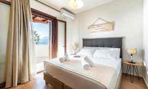 Makuuhuone, jossa on parivuode, koristeellinen seinämerkki, yöpöytävalaisimia ja avoin parvekkeen ovi, joka johtaa terassille. (Tekoälyn luoma teksti)