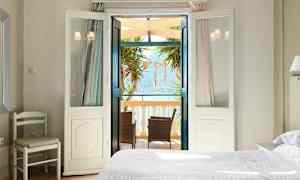 Vaalea makuuhuone, jonka avautuvat ovet johtavat parvekkeelle, jossa on huonekaluja ja näkymä merelle. (Tekoälyn luoma teksti)