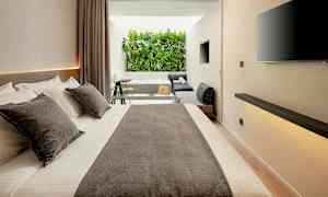 Moderni hotellihuone, jossa suuri sänky, oleskelutila ja näkymä vehreään ympäristöön. (Tekoälyn luoma teksti)