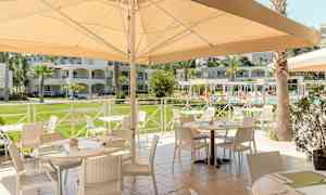 Ulkoilmaravintola, jossa on kalustettuja pöytiä lähellä uima-allasta ja ympäröiviä rakennuksia. (Tekoälyn luoma teksti)